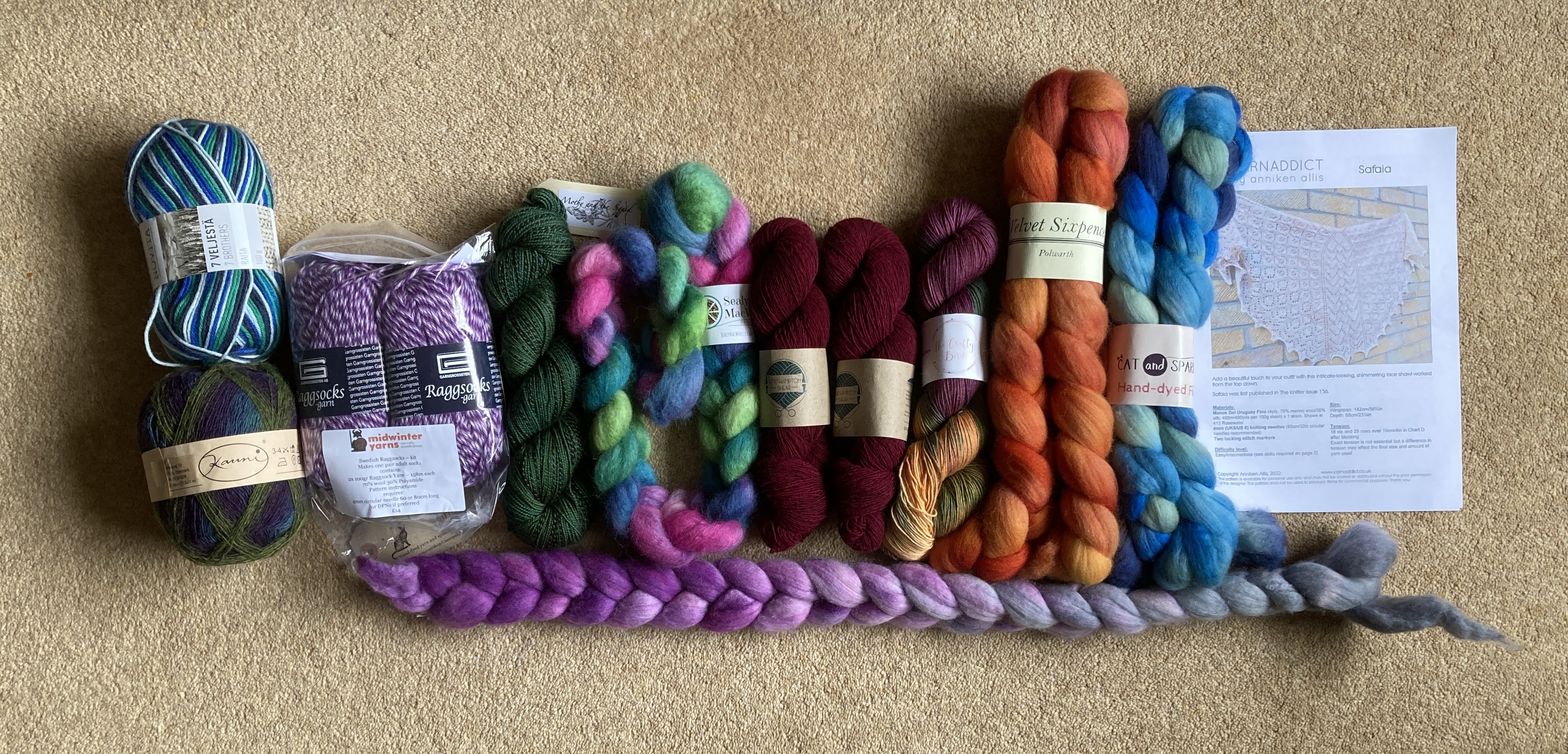 A very colourful range of fibre braids, skeins and balls of yarn and a knitting pattern laid out side by side