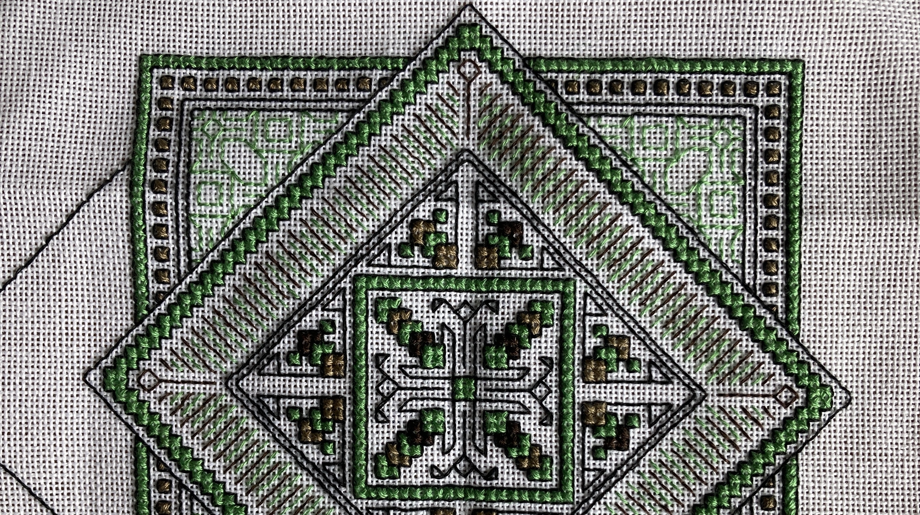 The top part of a partly completed blackwork and cross-stitch embroidery. Four colours are used, green, black and two shades of brown, and it is a geometric pattern based on nested squares at 45 degree angles to each other.