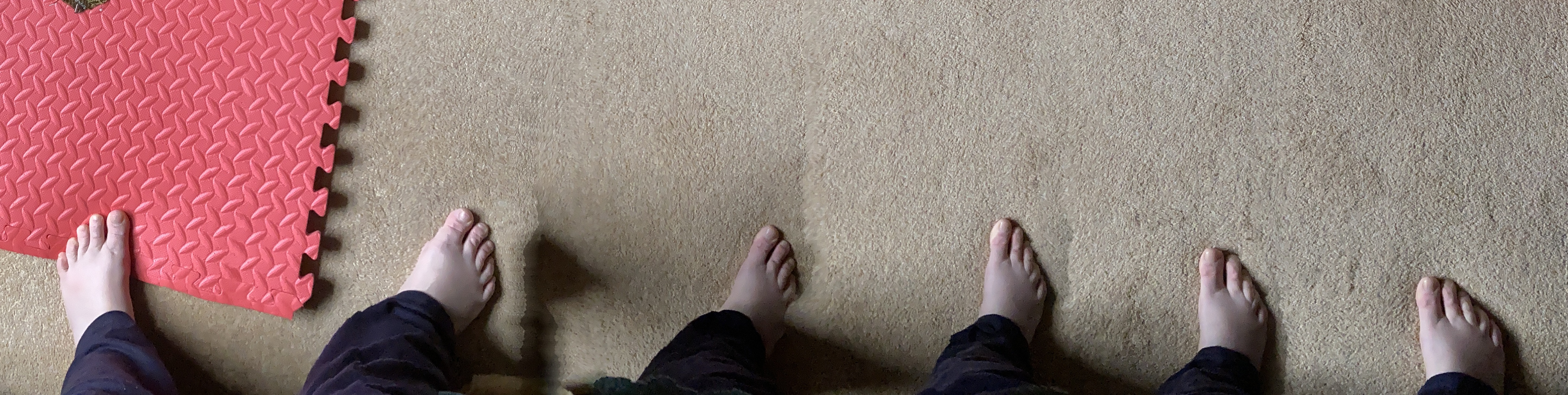 A panoramic photo showing one left foot and five right feet on a pale gold carpet. The left foot is just touching a red foam mat.