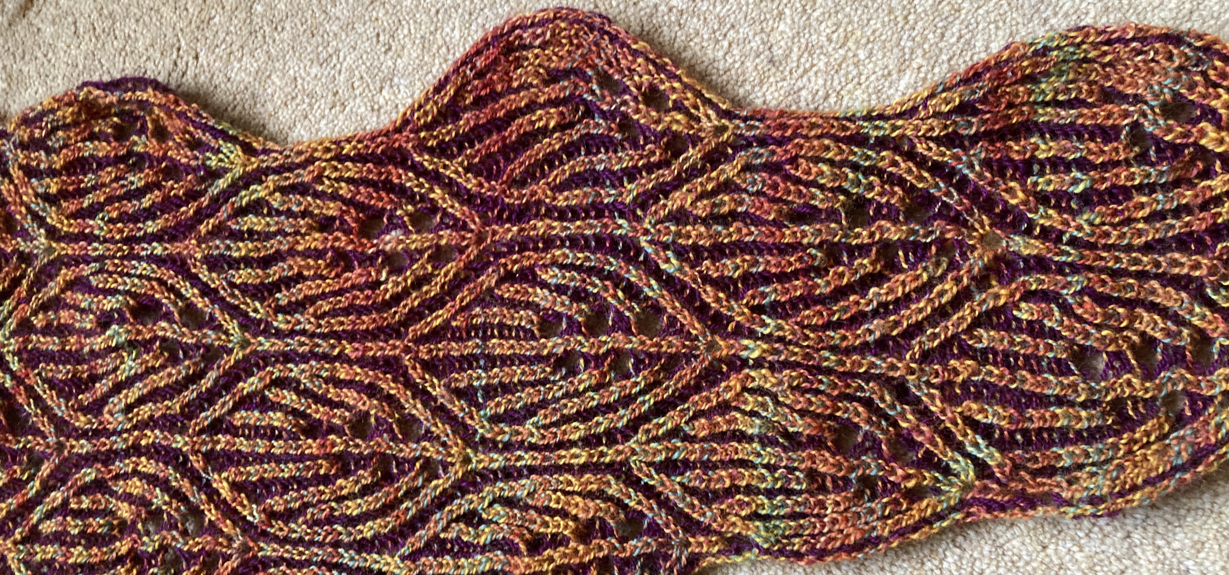 A close up of knitted brioche in fiery autumnal colours. The pattern has a motif of interlocking leaves.